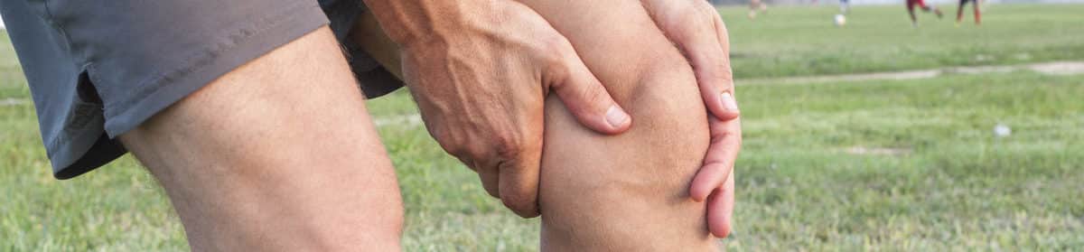 Closeup of athletic Caucasian man holding his painful knee on soccer field